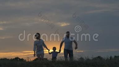 幸福的一家人在日落时在田野里奔跑。 夏夜一家人的剪影。 爱家庭的概念